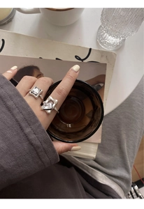 Detailed view of silver rings with square zircon on model hand against magazine backdrop