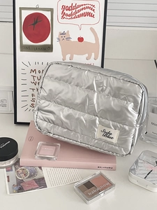 Macro view of silver quilted puffer cosmetic bag with Soda Blue label on table