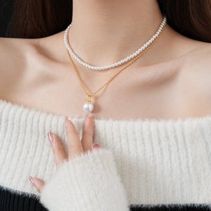 Close-up of double-layered pearl necklace with golden D-shaped pendant and beaded chain