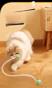Close-up of cat catching a green silicone bouncy ball toy with brown feathers on a wood floor