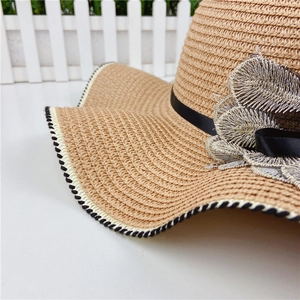Detail of wide brim straw hat featuring leaf embroidery and black ribbon bow decoration