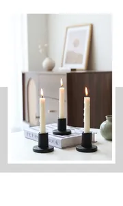Detail of minimalist black matte candle holders with white pillar candles on a table
