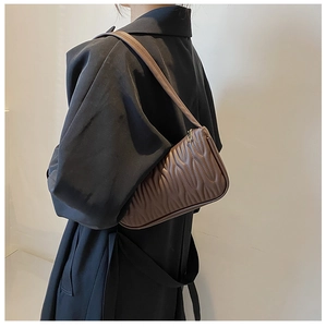 Brown pleated underarm bag worn with black coat showing stylish shoulder fit and texture