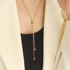 Close-up of a gold Y-shaped tassel necklace with metal beads on a model wearing a blazer