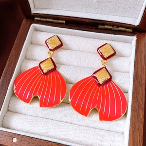 Detailed shot of red enamel fishtail fan earrings on a cream jewelry box cushion