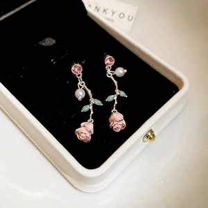Macro detail of enamel rose earrings with pink petals, green leaves, and pearl drop