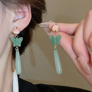 Detailed shot of pink cat-eye stone earrings with green butterfly and water drop charms
