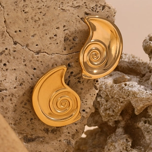 Macro shot of gold-plated cochlea spiral stud earrings on natural textured rock background