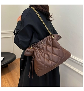Detail of a brown quilted leather bucket bag with gold chain strap and drawstring base