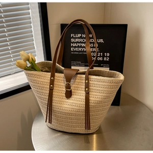 Detailed close-up of straw woven tote bag with brown leather straps on metal table