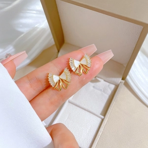 Detailed close-up of bow-knot gold earrings with white micro-paved crystals held by hand