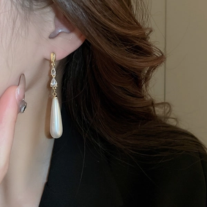 Détail de boucles d'oreilles dorées avec cristaux de zircon et longues perles pendantes