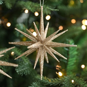 Sparkling gold star ornament on Christmas tree branch with warm bokeh background