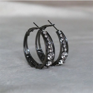Detailed close-up of gunmetal hoop earrings with clear inlaid zircons on faux fur background