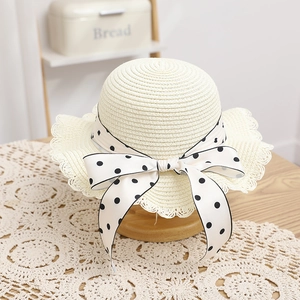 Close-up of beige woven straw hat with lace edges and a polka dot ribbon bow