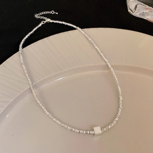 Close-up of a silver beaded necklace with a minimalist square pendant on a beige dish