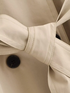 Close-up of khaki trench coat waist belt knot and dark brown button detail