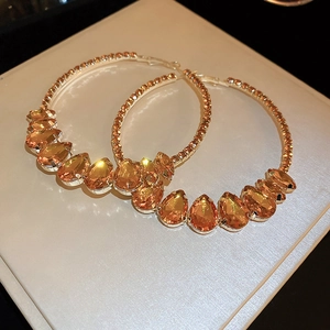 Vue détaillée de créoles dorées avec cristaux gouttes orange et pavage de diamants fins