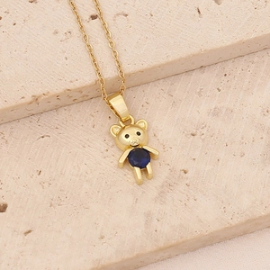 Detail of a golden bear necklace with a round blue gemstone on a textured stone base