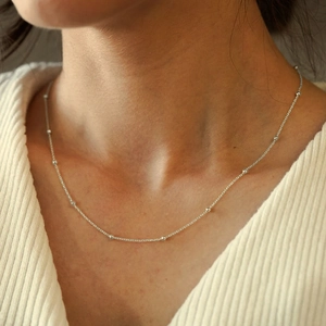 Close-up of minimalist silver stainless steel beaded chain necklace on a model's neck