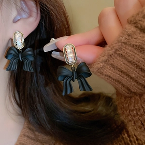 Close-up of black matte bow earrings with gold frames and sparkling zircon inlay
