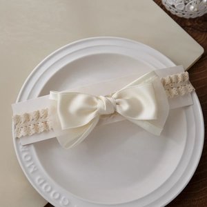 Bandeau bébé en dentelle avec grand nœud blanc cassé sur une assiette décorative