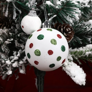 Close-up of white Christmas ornaments with red and green glitter dots on a snowy tree