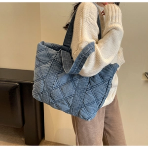 Détail du grand sac cabas en denim bleu matelassé porté à l'épaule par un mannequin