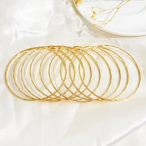 Detail shot of ten gold-tone slim bangles set on elegant white silk fabric