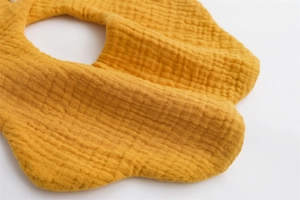 Close-up of ginger yellow petal-shaped muslin cotton baby bib with soft wrinkled texture