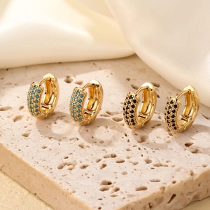 Boucles d'oreilles huggies en or avec pierres de zircon bleu ciel et noires sur marbre