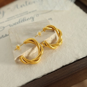 Elegant gold twisted hoop earrings displayed on decorative textured paper background