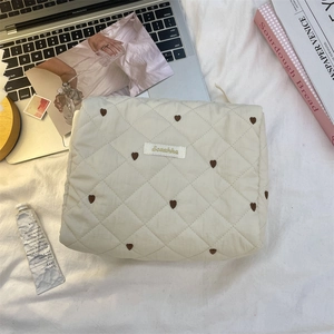 Nahaufnahme cremefarbene gesteppte Kosmetiktasche mit brauner Herzbestickung und Label