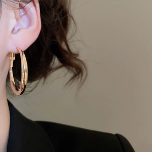 Close-up of a thick gold C-shaped hoop earring with a polished metallic finish on model