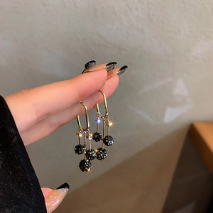 Détail de longues boucles d'oreilles dorées avec globes en strass noirs style franges