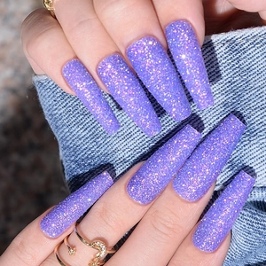 Close-up of long purple glitter press-on nails on denim fabric with sparkly sequins