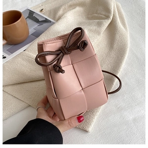 Detail of pink hand-woven bucket bag featuring a brown knotted strap and leather texture