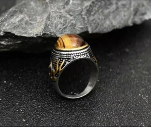Retro men's tiger eye ring with gold wave patterns on a dark rocky background