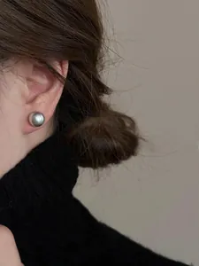 Dettaglio di un orecchino a bottone con perla grigia indossato da una modella elegante