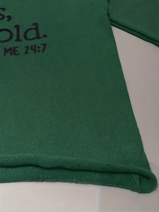Détail du pull en maille verte montrant la texture du col en V et l'imprimé S, Old. ME 24:7