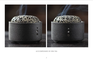 Close-up of black ceramic incense burner with elegant hollow leaf pattern metal lid and smoke