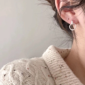 Close-up of a minimalist silver geometric hoop earring worn with a beige knit sweater
