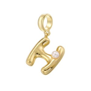 Vue macro d'un pendentif en forme de lettre H dorée avec une perle blanche sur fond blanc