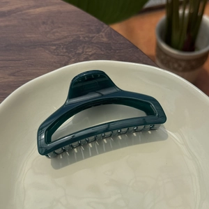 Detail view of a 10cm dark green perfume bottle hair claw on a beige ceramic plate