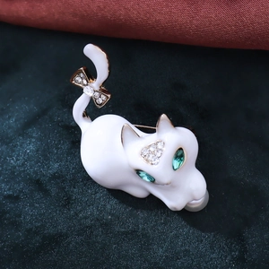 Macro shot of white enamel cat brooch with green gem eyes and a sparkling bow detail