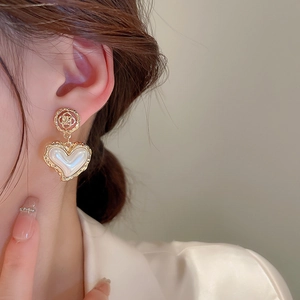 Detail of vintage heart earrings with pearl inlay and golden flower stud on model
