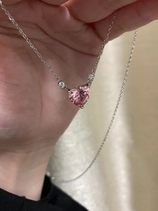Macro detail of pink heart pendant with silver chain held in hand for real-life texture