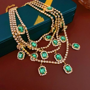 Macro detail of layered gold necklace featuring emerald green gems on luxury gift box