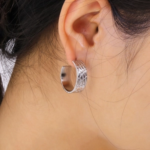 Detailed view of a silver C-shaped earring with embossed diamond texture on model