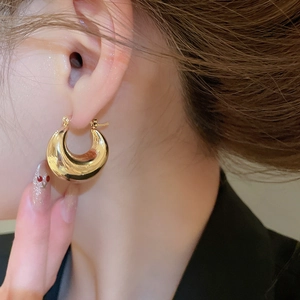 Close-up of chunky gold C-shaped hoop earrings on model featuring a polished metallic finish